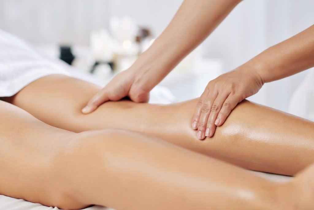 Hands of massage therapist massaging legs of young woman in spa salon